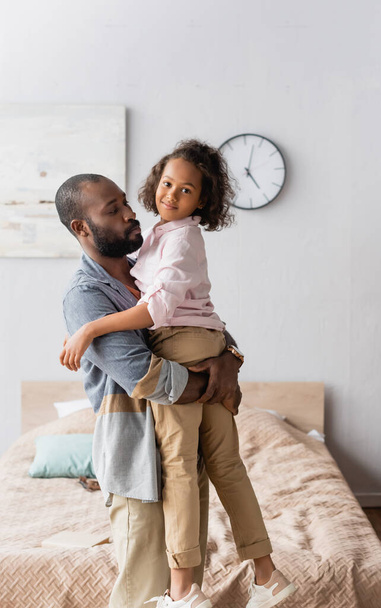young african american father holding daughter on hands while she looking at camera - Foto, Bild