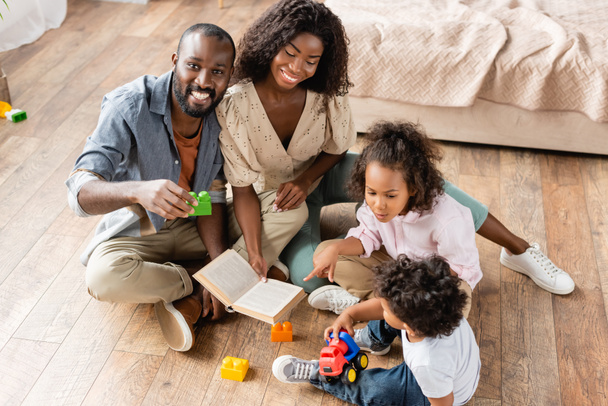 high angle view of african american family sitting on floor with building blocks and book - 写真・画像