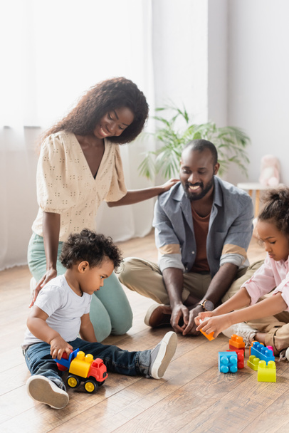 young african american parents in casual clothes near children playing on floor with building blocks - 写真・画像