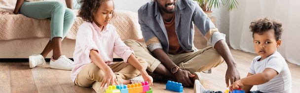 vista ritagliata di bambini afroamericani con padre che gioca con cubi di legno sul pavimento, colpo panoramico - Foto, immagini
