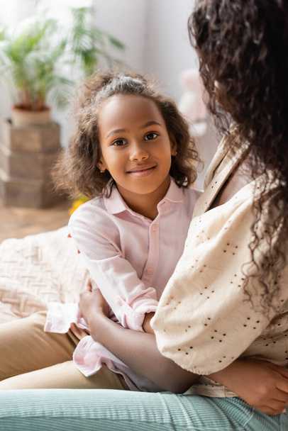 african american girl embracing mother while looking at camera at home - Photo, image