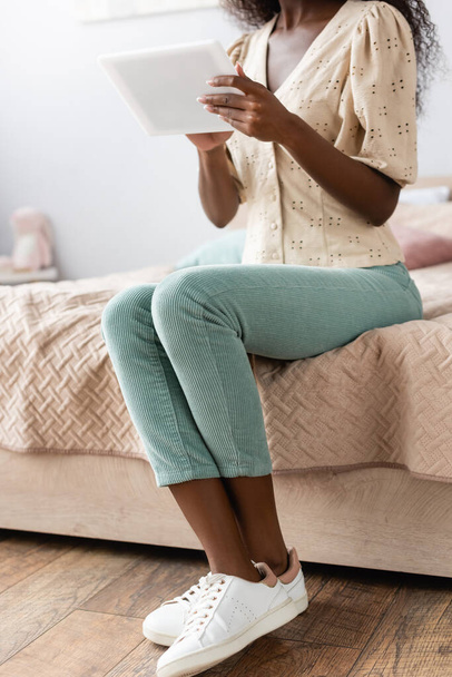 cropped view of african american woman in blouse and pants using digital tablet in bedroom - Fotó, kép