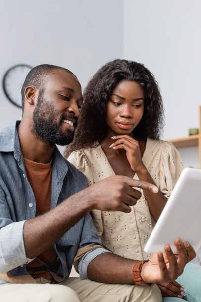 Genç Afro-Amerikalı adam parmak ucunda dijital tableti gösteriyor. Düşünceli karısının yanında. - Fotoğraf, Görsel