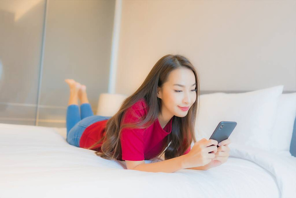 Ritratto bella giovane donna asiatica uso smart cellulare sul letto in camera da letto interno - Foto, immagini