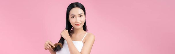 Portrét krásné mladé asijské ženy česání její vlasy, pohled na kameru a úsměv - Fotografie, Obrázek