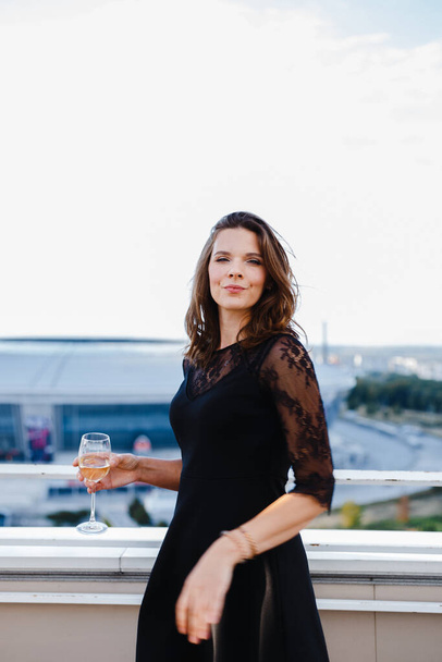 mujer con una copa de vino en el balcón sobre el fondo de la ciudad - Foto, Imagen