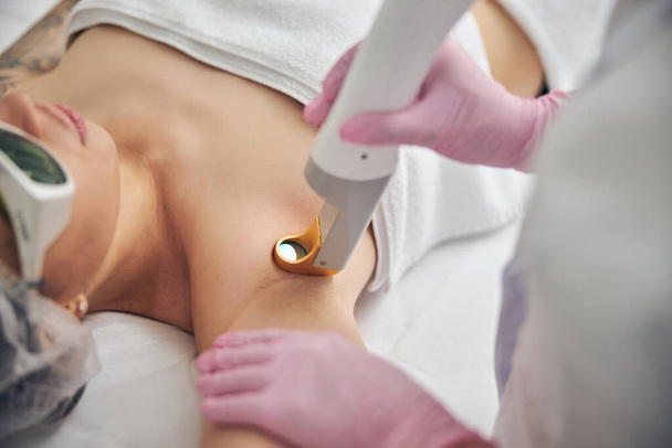 Дерматолог направляет концентрированный лазерный луч на подмышку пациента - Фото, изображение