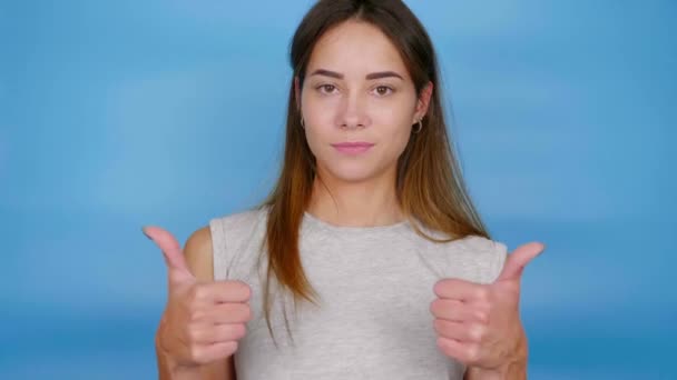 Positive woman in gray t-shirt raises hands, shows thumbs up, likes and smiles - Footage, Video