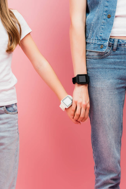 vue recadrée de mère et fille en jeans et smartwatches tenant la main sur rose - Photo, image