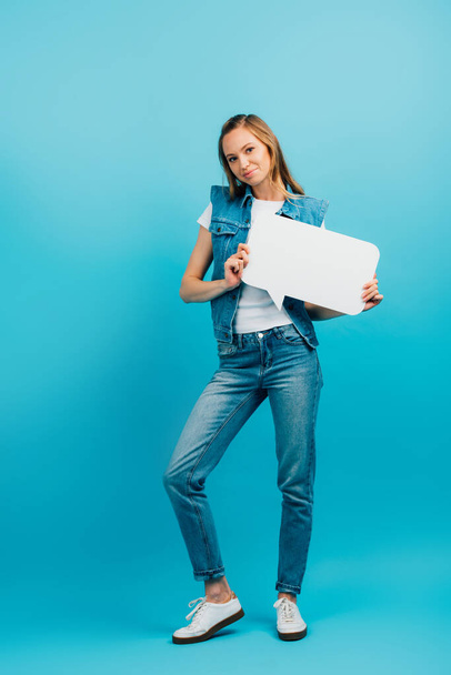 full length view of woman in denim vest and jeans holding speech bubble on blue - Foto, Bild
