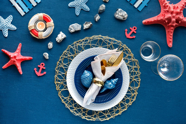 Columbus Day or Summer birthday lunch table, blue white with red. Flat lay, contemporary nautical table setting with sea decorations on classic blue linen textile. Plates, golden cutlery, sea shells - Zdjęcie, obraz