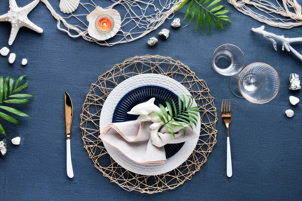 Contemporary nautical table setting with sea decorations on classic blue linen textile. Plates, golden cutlery, utensils. Top view, Columbus Day, Summer birthday lunch table, blue, white and green. - Valokuva, kuva