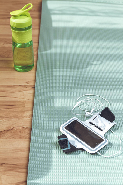 Wasserflasche und Smartphone auf Matte auf dem Boden. Den Körper während der Zeit der Selbstisolation in guter Form zu halten. Sport zu Hause treiben - Foto, Bild