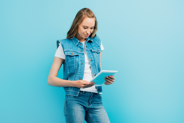 focused woman in denim clothes using digital tablet isolated on blue - Foto, Imagem