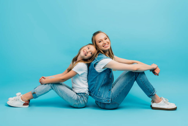 child in white t-shirt and jeans sitting with mother in denim clothes on blue - Photo, Image