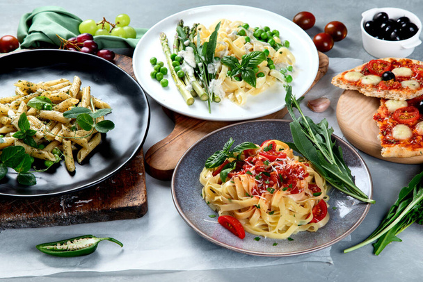 Variety of homemade prepared vegan pasta, pizza and snacks on gray background. Italian cuisine.  - Foto, Imagen
