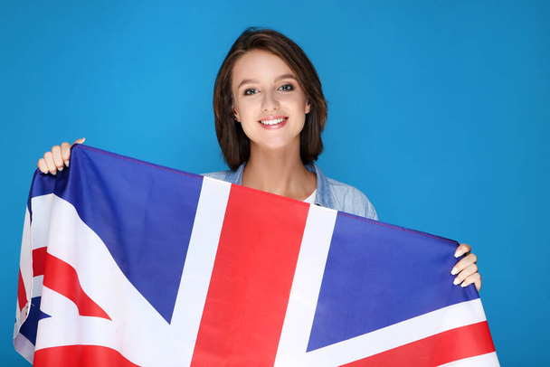 Beautiful young woman holding british flag on blue background - Фото, изображение