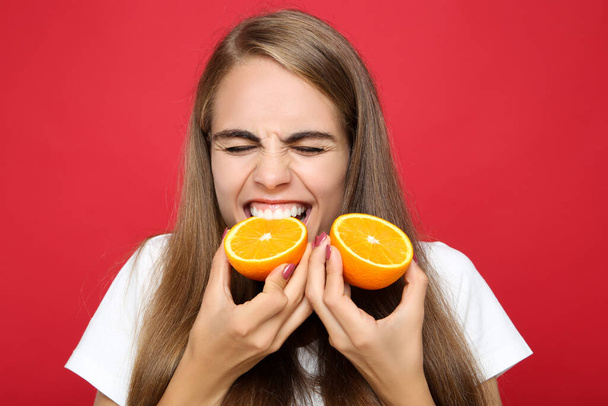 Young girl eating fresh orange fruit on red background - Фото, зображення