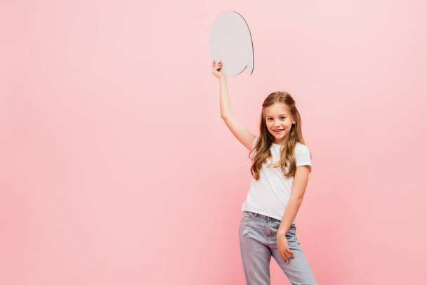 child in white t-shirt and blue jeans holding thought bubble while looking at camera isolated on pink - Photo, Image