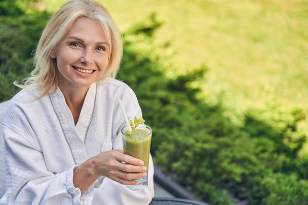 Smiling woman wearing white soft bathrobe standing in outside - Foto, afbeelding