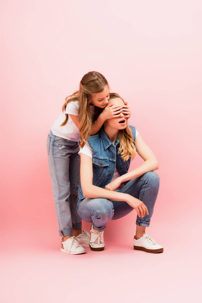 child in jeans covering eyes of mother wearing denim clothes on pink - Valokuva, kuva
