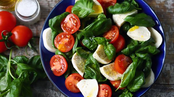 Caprese-salaatti sinisellä lautasella. Terveellinen salaatti tomaattien, basilikan ja mozzarellan kanssa. - Valokuva, kuva