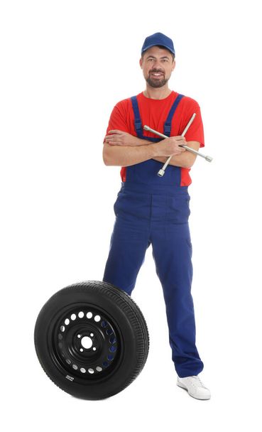 Full length portrait of professional auto mechanic with lug wrench and wheel on white background - Zdjęcie, obraz