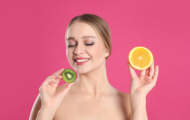 Young woman with cut kiwi and orange on pink background. Vitamin rich food - Фото, зображення