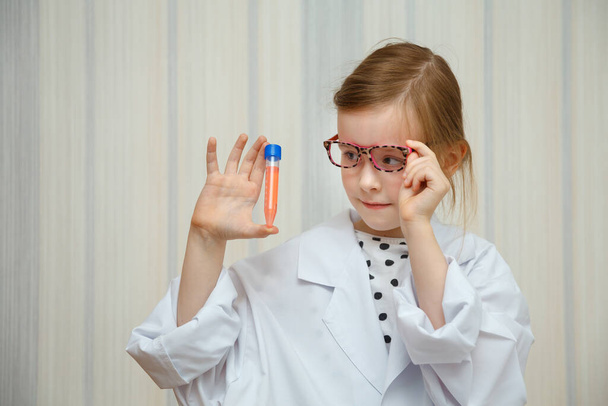 Klein meisje in een doktershok onderzoekt reageerbuisjes met testen. Educatief medisch spel. - Foto, afbeelding