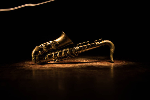 Music concept. Saxophone jazz instrument. Alto gold sax miniature with colorful toned light on foggy background. Saxophone music instrument in lowlight. Selective focus - Φωτογραφία, εικόνα