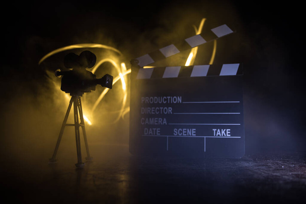 Movie concept. Miniature movie set on dark toned background with fog and empty space. Silhouette of vintage camera on tripod and clapboard. Selective focus - Photo, Image