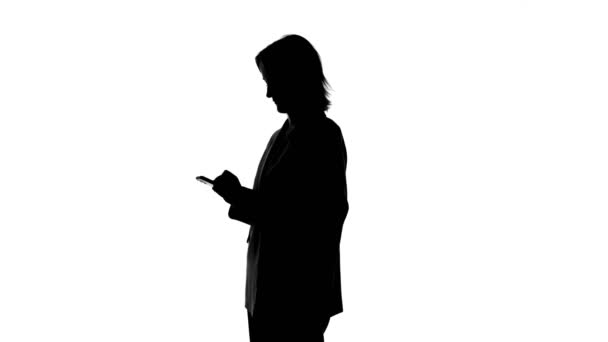 Video of womans silhouette in suit jacket with smartphone - Footage, Video
