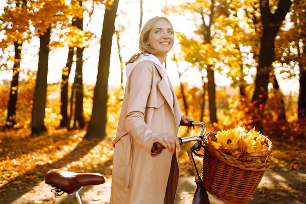 Stylish woman with a bicycle enjoying autumn weather in the park. Beautiful Woman walking  in the autumn forest. - Φωτογραφία, εικόνα