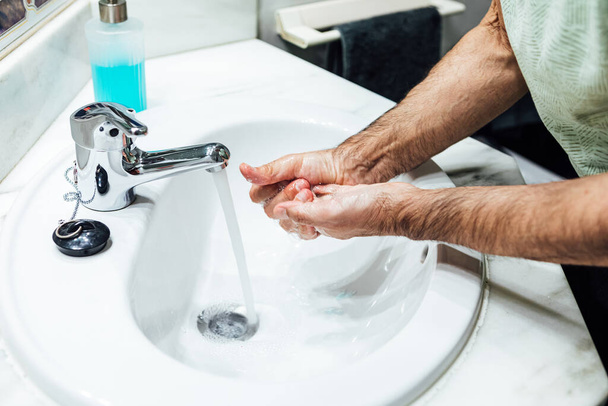 Mains d'un homme se lavant avec du savon dans la salle de bain afin de ne pas être infecté par le coronavirus. Concept covid. - Photo, image