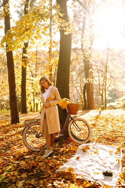 Stylish woman with a bicycle enjoying autumn weather in the park. Beautiful Woman walking  in the autumn forest. - Valokuva, kuva