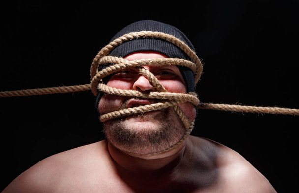 Portrait of binded fat man in cap with rope on face - Photo, Image