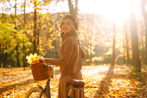 Stylowa kobieta z rowerem ciesząca się jesienną pogodą w parku. Piękna kobieta spacerująca w jesiennym lesie. - Zdjęcie, obraz