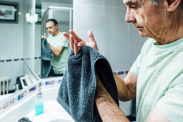 男はコロナウイルスに感染するのを避けるために石鹸でそれらを洗浄した後、バスルームで手を乾燥させます.covidの概念. - 写真・画像