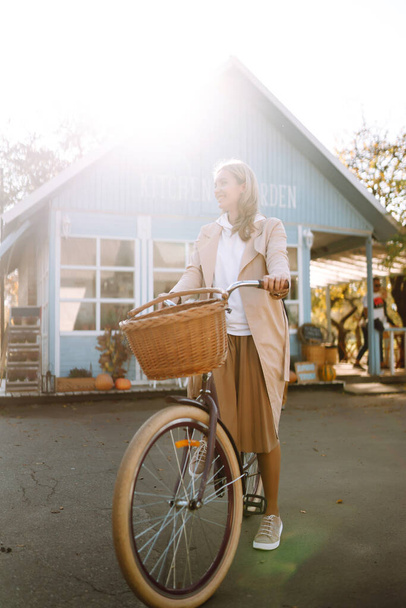 Stylowa kobieta z rowerem ciesząca się jesienną pogodą na tle niebieskiego domu. Relaks, radość, samotność z naturą. - Zdjęcie, obraz