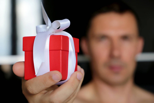 Gift box in male hand close up, man giving present in red packaging with white ribbon. Valentine's day surprise, birthday celebration - Fotoğraf, Görsel