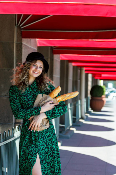 Portrait pretty woman with baguette in hands on street. Girl dressed in French style show emotion. Sunny day. Female in stylish clothes holding fresh baguettes. Place for inscription or logo - Foto, afbeelding