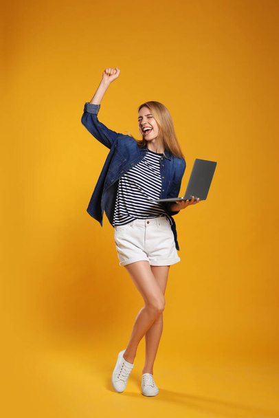 Full length portrait of emotional woman with modern laptop on yellow background - Fotografie, Obrázek