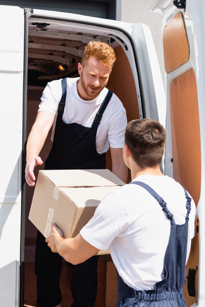 Enfoque selectivo del cargador que da caja de cartón a sus colegas mientras descarga el camión al aire libre  - Foto, imagen