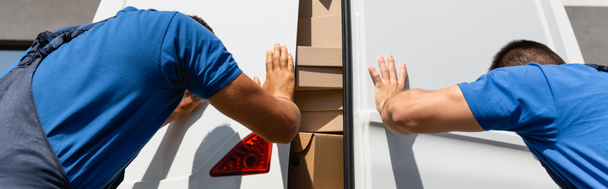 Horizontal crop of movers in uniform closing cardboard boxes in truck on urban street  - Photo, Image