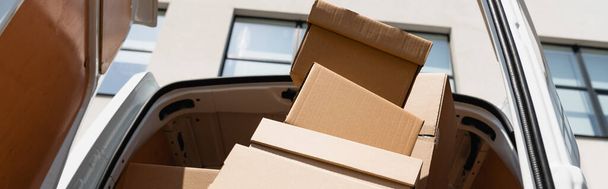 Foto panorámica de cajas de cartón en camión con puertas abiertas en calle urbana  - Foto, Imagen