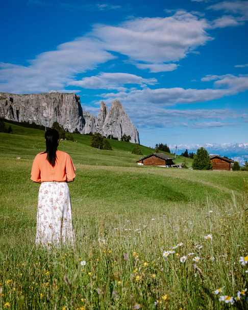 женщина на отдыхе в Доломитовых Альпах Италии, Альпе ди Siusi - Сейзер Альм с Sassolungo - Langkofel горной группы на заднем плане на закате. Желтые весенние цветы и деревянные шале в Доломитах, Трентино - Фото, изображение