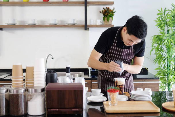Souriant asiatique jeune homme barista verser du lait frais dans le café glacé latte art selon la commande du client au comptoir bar dans le café. - Photo, image