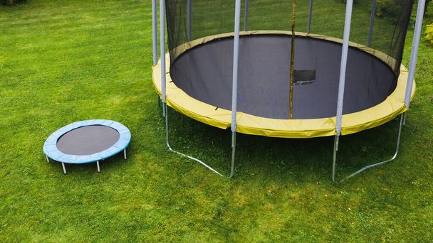 mała trampolina w pobliżu dużej z okrągłą matą, porównanie rozmiarów, zielone tło trawnika - Zdjęcie, obraz