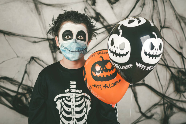 Happy Halloween. kid wearing medical mask in a skeleton costume with halloween balloons - Photo, Image