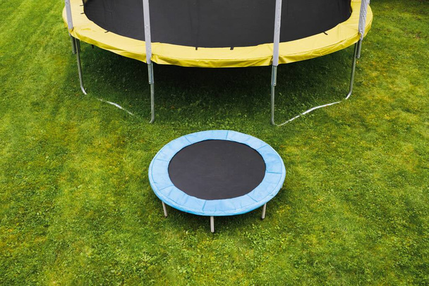malá trampolína poblíž velké s kruhovou rohožkou, porovnání velikosti, zelené pozadí trávníku - Fotografie, Obrázek